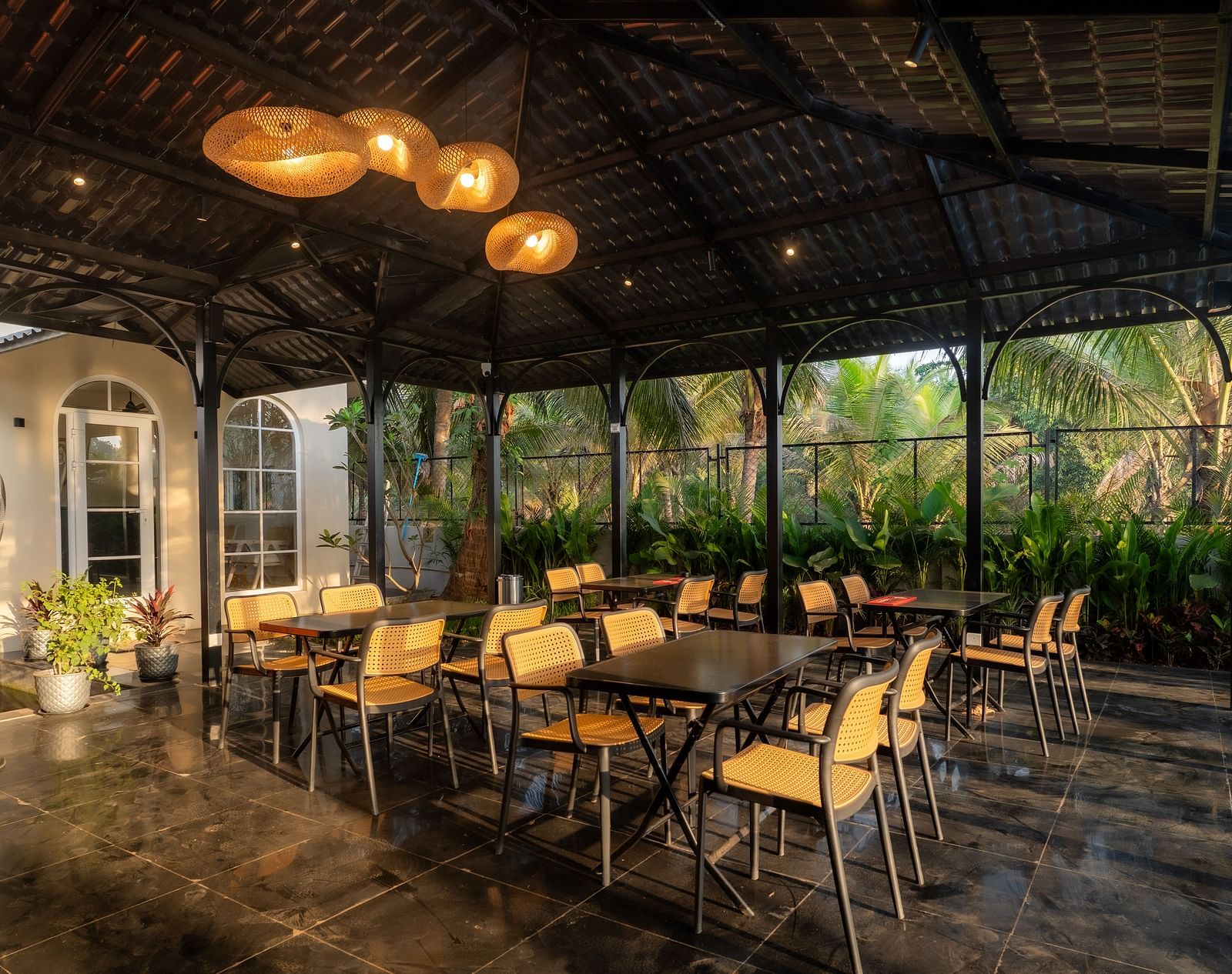 Spacious covered dining area with stylish lighting, offering views of the garden and swimming pool at Kssemya.