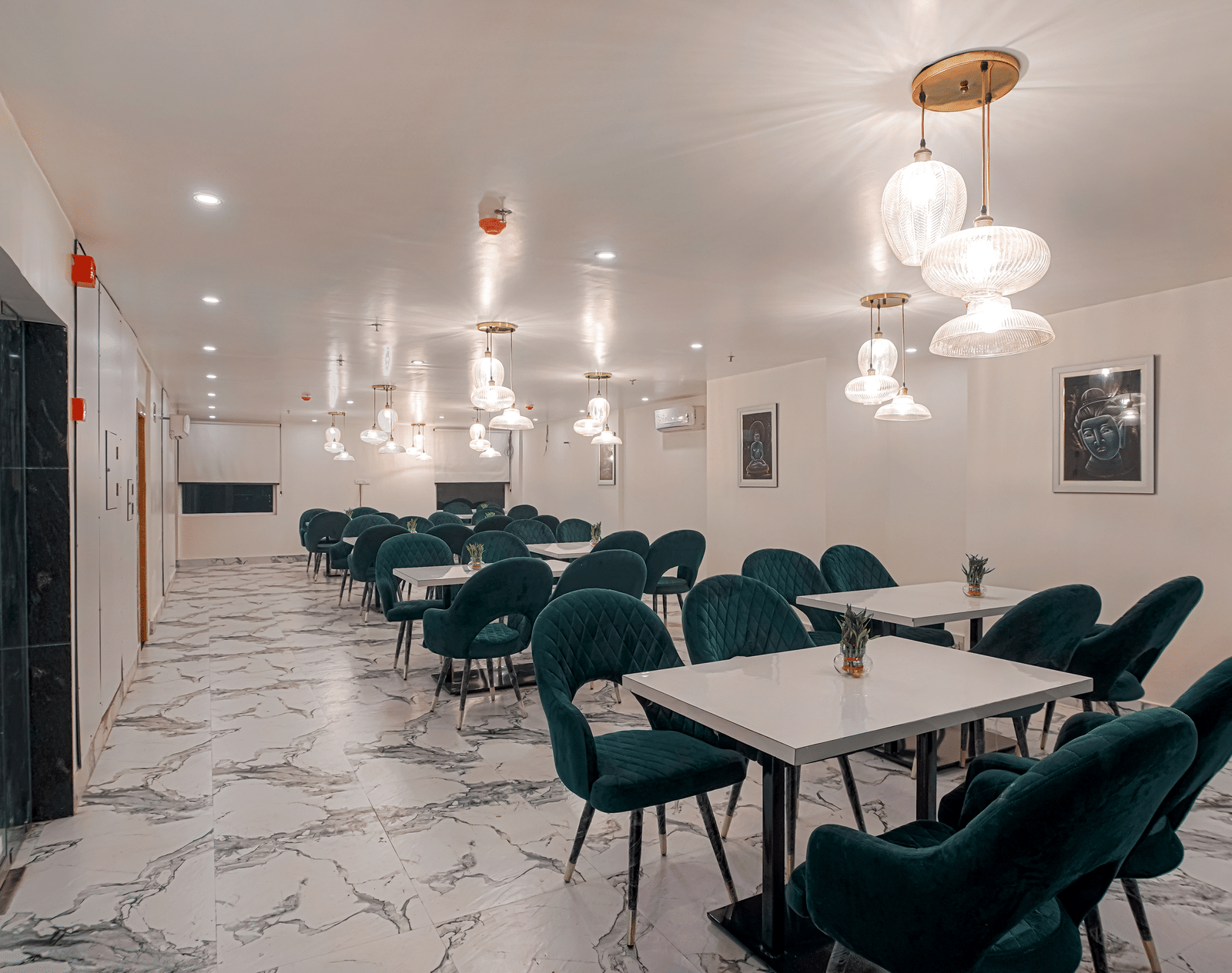 A modern white dining hall featuring elegant glass ceiling lights, neatly arranged tables and chairs at Perfectstayz Premium Varanasi.