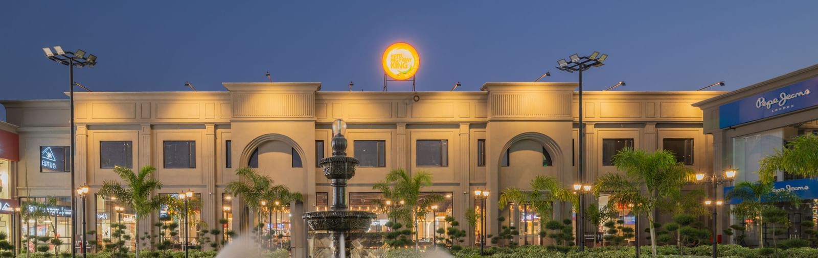 Fountain and courtyard area at Hotel Highway King, Kishangarh with the main building illuminated at dusk.