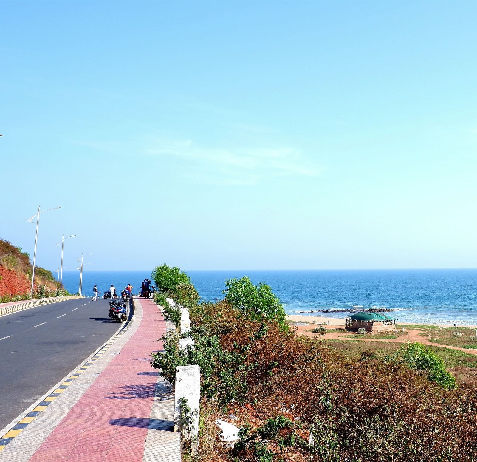 A road next to a beach with vegetation next to the road and the ocean in the distance