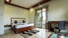 Bedroom at Magnus Vosiv Suites, Kalyani Nagar featuring double size bed, bedside table, work desk and chair, and an attached balcony.