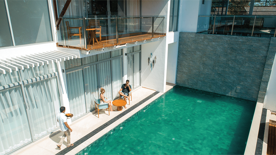 a clear greenish-blue pool at Beacon by the Bay Villas & Suites by The Clarks, Dondra featuring people chilling at the deck as the waiter is walking to them with food