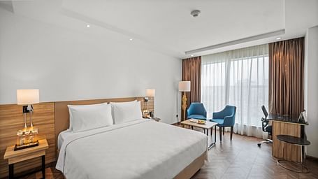 An image of a king size bed and chairs next to a huge window at Grand Vijayawada by GRT Hotels.