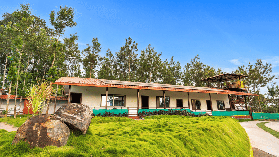 Hatti Eden Coorg resort exterior with terracotta-roofed cottages, lawn, and eucalyptus trees under a clear blue sky