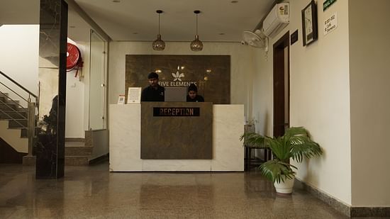 Reception at Five Elements Hotels, Haridwar, featuring a flower pot in the corner and a staircase on the other side