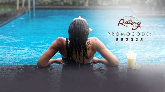 A woman relaxing at the edge of a pool in the rain with a tropical drink beside her, creating a serene and indulgent monsoon vibe. Promotional offer text on the image reads, Rainy Bliss – Promocode: RB2025