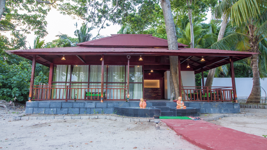 Tropical wooden pavilion with red roof and veranda, surrounded by lush trees, featuring a red carpet walkway leading to the entrance - Summer Sand Beach Resort And Spa, Neil island