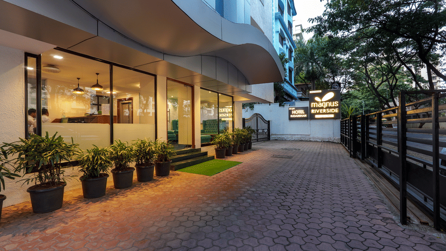 Driveway or pavement at Magnus Riverside, Kalyani Nagar featuring flower pots on one side. The ground floor of the building is made of glass walls through which we can see the interiors.