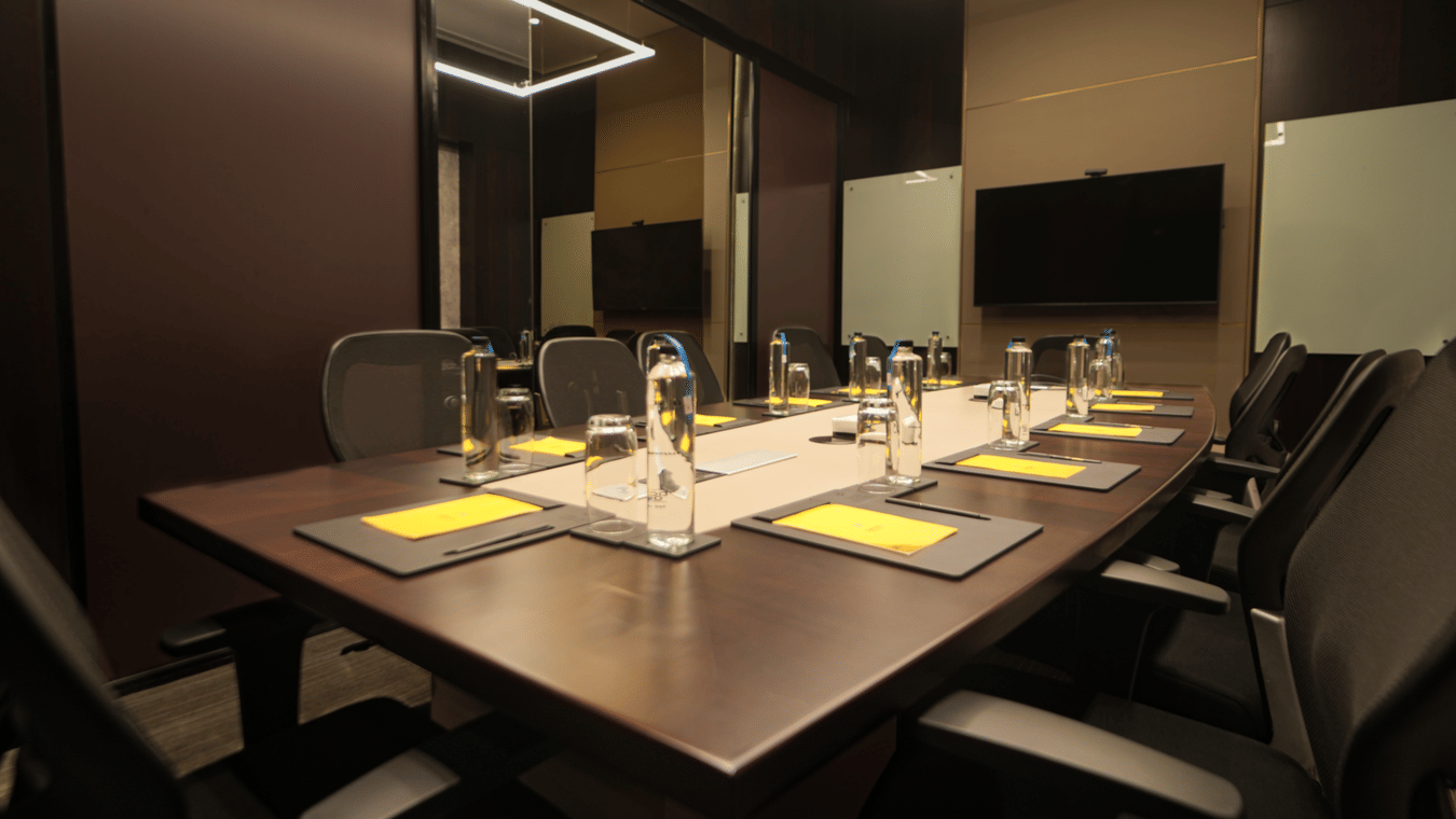 A rectangular table set with placemats cutlery and chairs arranged inside a meeting hall at The Suryaa, New Delhi.