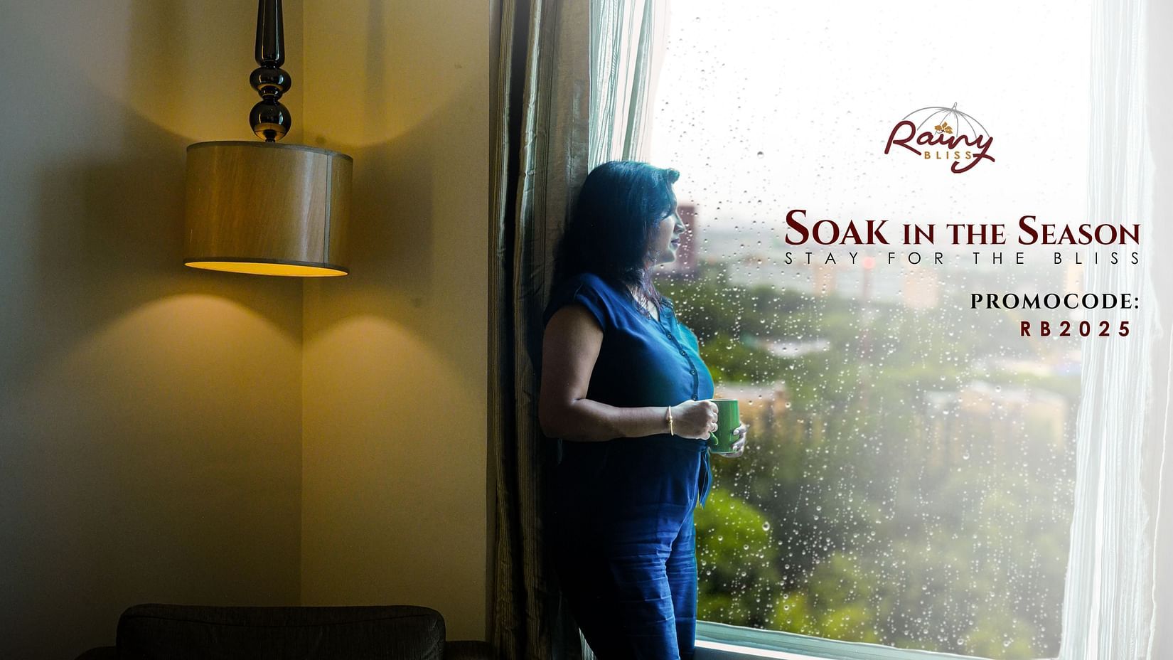 A woman enjoying a warm beverage while gazing out of a hotel window on a rainy day, evoking comfort and tranquility. Promotional offer text on the image reads, Rainy Bliss – Soak in the Season. Stay for the Bliss. Promocode: RB2025