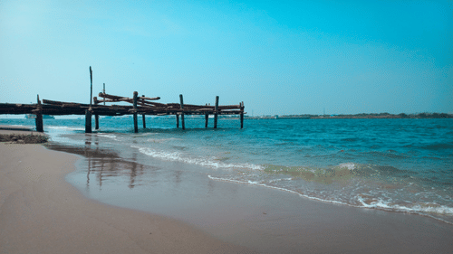 An overview of Fort Kochi Beach with a wooden Pier in view and waves overlapping on the beach.