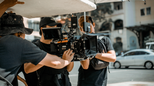 A group of people operating a professional camera on a street with buildings in the background.