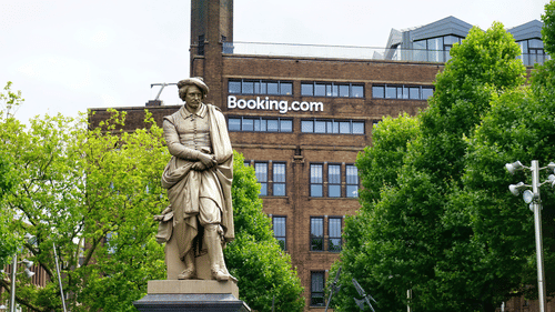 a statue with booking.com signage on a building with a brick exterior