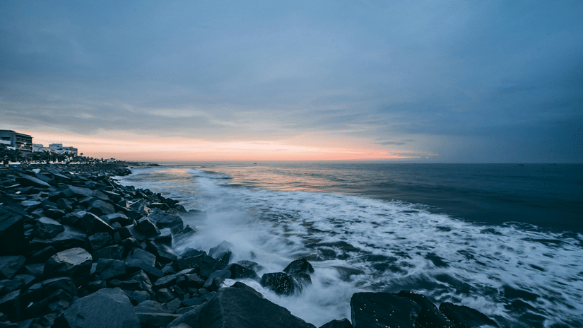 A view of Promenade Beach in Pondicherry with rocks scattered along the shoreline and waves hitting them as seen during dawn.