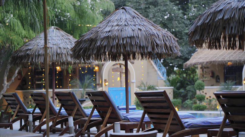 Row of wooden sun loungers and thatched umbrellas beside the swimming pool at Themis Mudhouse – A Nature Retreat Resort & Wellness.