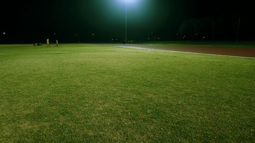 A large and empty lawn illuminated by a lampost during the night.