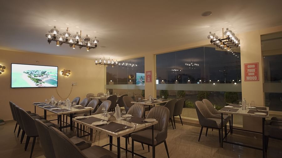 A stylish restaurant with elegant grey chairs, marble tables, and soft lighting. Large windows offer a view of the outside greenery at Citrus Classic Resorts and Spa Mahabalipuram ECR