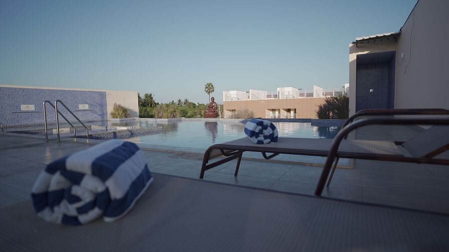 Lounge area arranged on the pool deck at Citrus Classic Resorts and Spa Mahabalipuram ECR with bath towels placed on the lounging chairs overlooking the pool on a sunny day