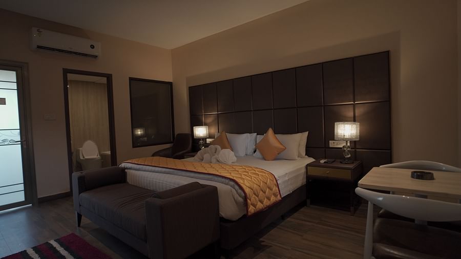 A dimly lit Premium Room at Citrus Classic Resorts and Spa Mahabalipuram ECR featuring a plush bed with hand towels made into swans while the light is coming from the opaque door to the balcony