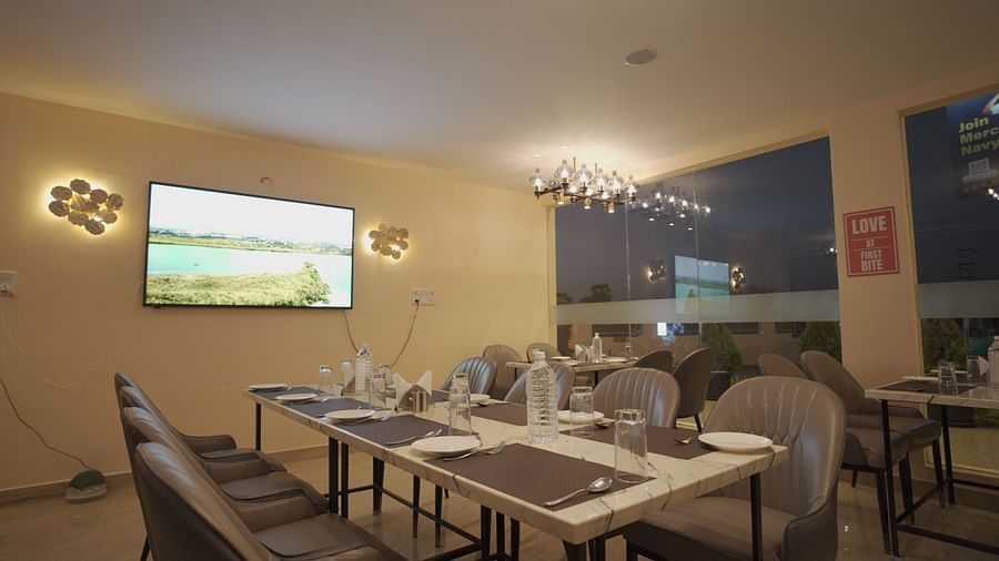 A modern restaurant with marble tables, grey chairs, warm lighting, and a TV. Glass windows offer a night view. Cozy and elegant at Citrus Classic Resorts and Spa Mahabalipuram ECR