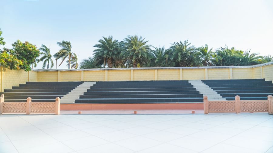 An image of stairs of amphitheatre where spectators sit and beyond that is a wall and trees bounding the entire  structure - The Garden Ananta Elite, Rajkot