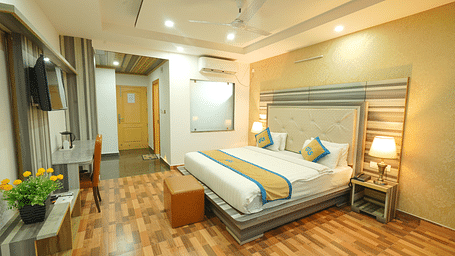 A wide angle shot of a spacious room featuring king size bed, television, wooden flooring, bed side lamp | DLS Hotel Shiva Sanctuary & Spa, Dharamshala