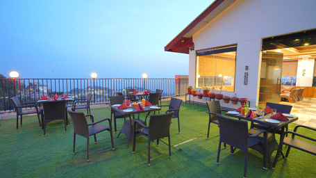 A rooftop restaurant with a scenic view. The restaurant has tables and chairs set up on a grassy area | DLS Hotel Shiva Sanctuary & Spa, Dharamshala