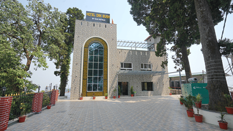 Front view of hotel exterior and courtyard bordered by trees at DLS Oak Bush, Mussoorie.   