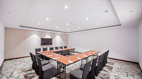 Grand Club Lounge II in Vijayawada arranged in a U-shaped meeting setup with wooden tables, comfortable seating, and a display screen - Grand Vijayawada by GRT Hotels