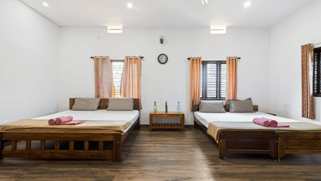 A Quad Room With Forest View in Hatti Eden Coorg featuring two wooden platform beds with white linens, each positioned under a window with light-colored curtains.