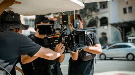 A team of film crew members are filming on a street with a camera and lighting equipment.