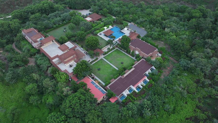 An aerial view of the resort buildings and central lawn nestled within a dense forest | Anandam Jungle Retreat Resort, Udaipur