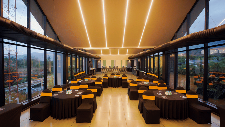 Blue Moon event hall at Darza Resorts with round banquet tables, black and orange seating, buffet counters and floor-to-ceiling windows overlooking the greenery in Coimbatore.