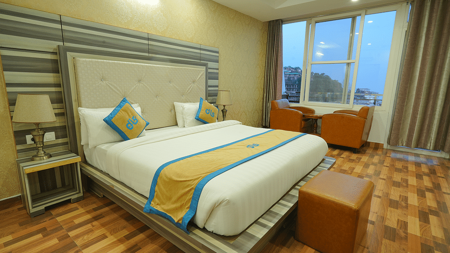 A cosy hotel room with a comfortable bed, a seating area with chairs, and a large window offering a view of the outdoors | DLS Hotel Shiva Sanctuary & Spa, Dharamshala