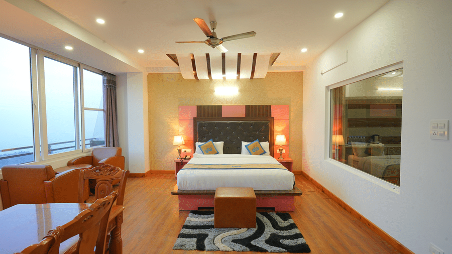 A spacious hotel room with a large bed, a seating area with a table and chairs, and large windows offering a view of the outdoors | DLS Hotel Shiva Sanctuary & Spa, Dharamshala
