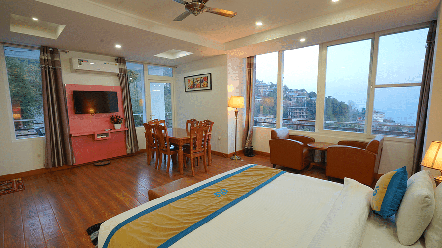 A spacious hotel suite with a king size bed, a seating area with a sofa and armchair, a dining table, and a flat-screen TV | DLS Hotel Shiva Sanctuary & Spa, Dharamshala