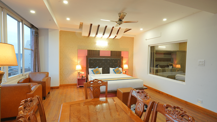 A side angle shot of the hotel suite with a king-sized bed, a seating area with a sofa, a dining table, and a flat-screen TV | DLS Hotel Shiva Sanctuary & Spa, Dharamshala