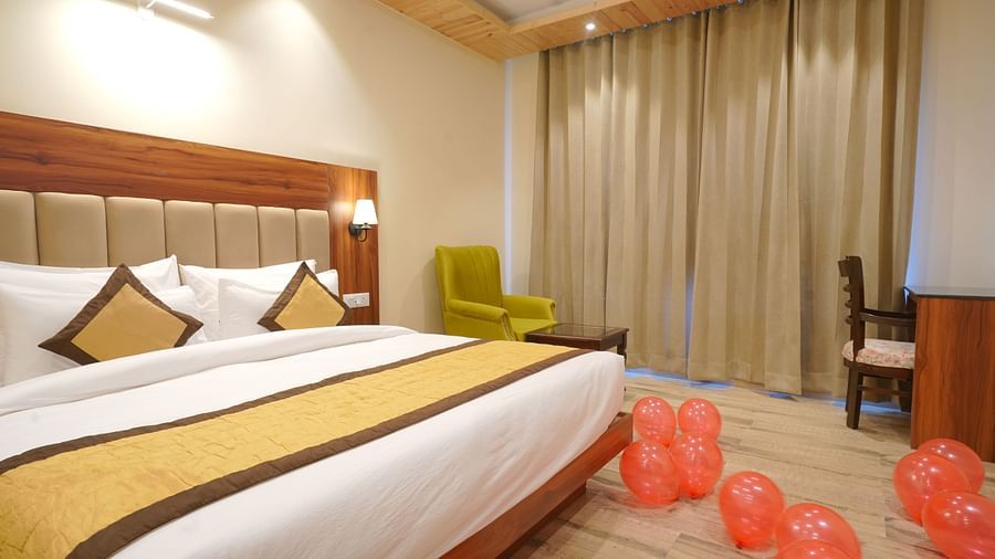 A large bed near a comfortable chair in Deluxe Room at DLS Oak Bush, Musssoorie.