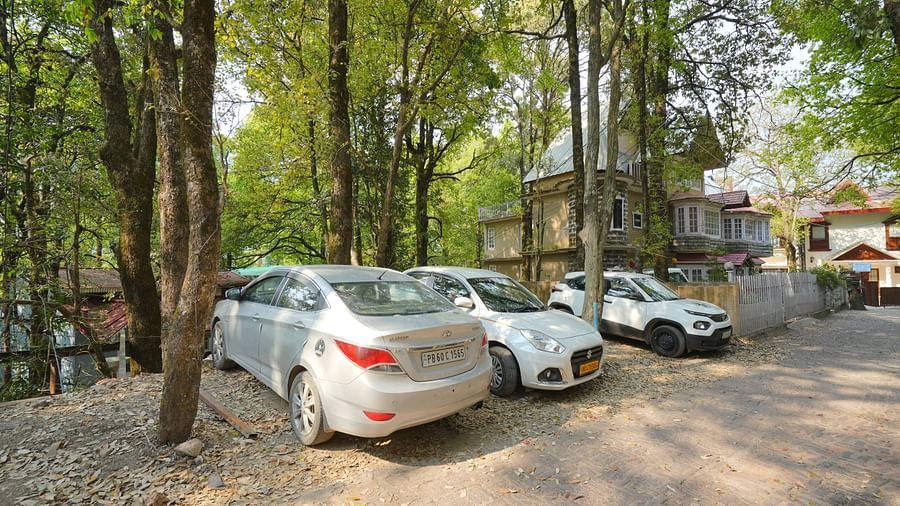 The parking area at DLS The Emerald, Nainital where three cars are parked surrounded by trees and greenery