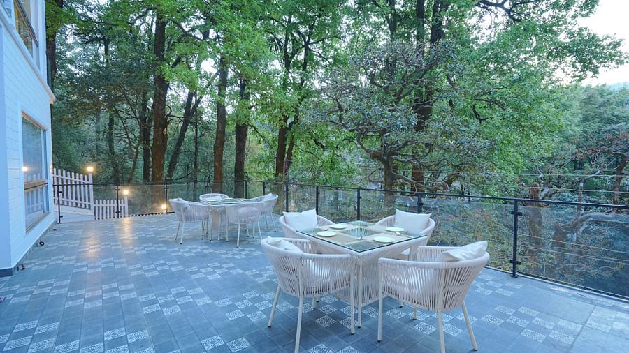 The deck at DLS The Emerald, Nainital featuring chairs and tables surrounded by trees
