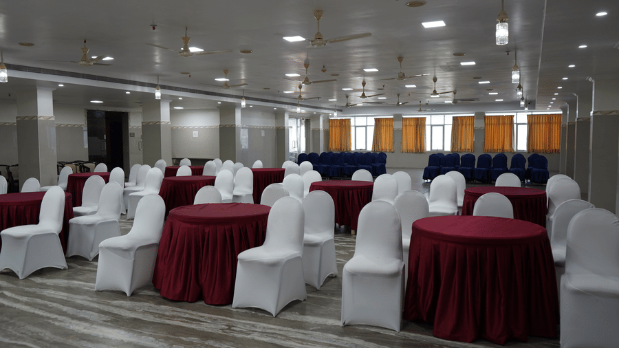 A wide banquet hall featuring round tables, covered chairs, and ceiling light fixtures across a tiled floor at DSF Grand Plaza, Tuticorin.