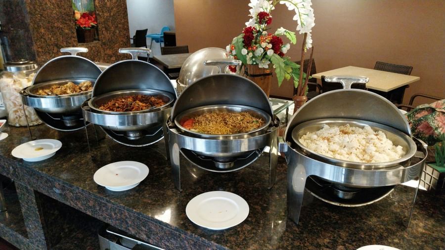 Multiple chafing dishes with various Indian curries and rice arranged on a marble buffet counter at Fireflies Resorts, Kabini.
