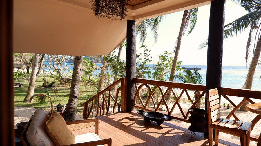 Private wooden veranda with cushioned seating, palm tree surroundings, and ocean views at Flower Island Resort Imperial Villa.