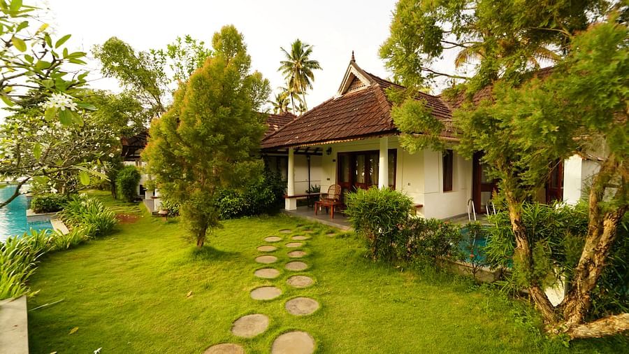 an image of an entrance of a cottage with walking steps surrounded by grasslands - Rhythm Kumarakom