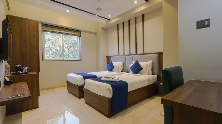 alt-text An image of a bedroom with twin beds, a wardrobe, flat TV screen, a work desk and chair, and a table where a tea and coffee maker is placed - Magnus Fortune House, Magarpatta