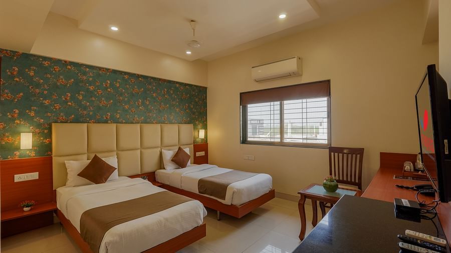 alt-text twin bed in a deluxe room with bright and vibrant colours with room amenities like television and air-conditioning - Magnus Square, Viman Nagar