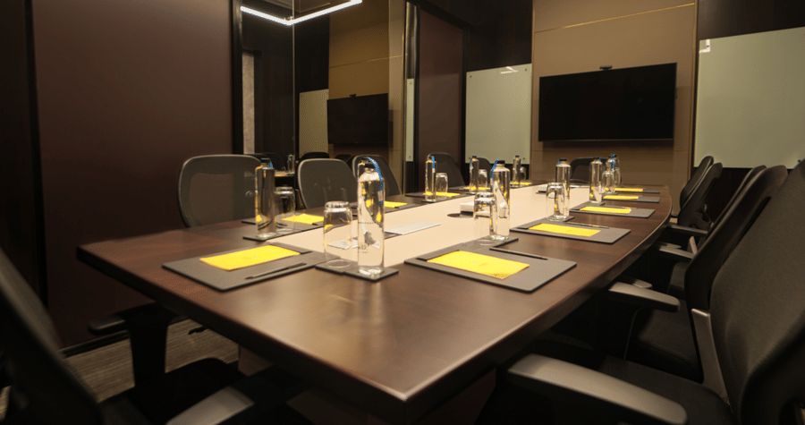 A rectangular table set with placemats cutlery and chairs arranged inside a meeting hall at The Suryaa, New Delhi.