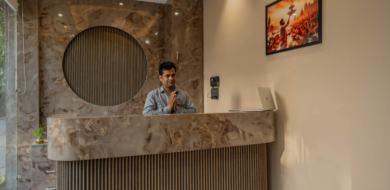 Hotel reception area with a contemporary wooden circular design element on the wall and a staff member standing behind the desk - Perfectstayz Value Aalaya Suites, Haridwar