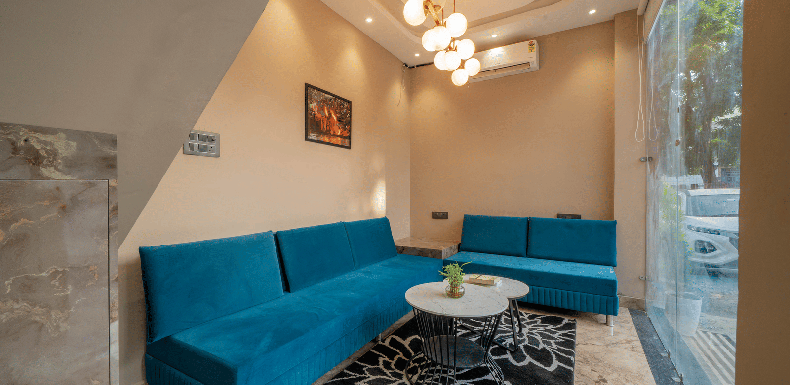 Modern lounge area with a bright turquoise sectional sofa, black and white rug, and overhead lighting - Perfectstayz Value Aalaya Suites, Haridwar