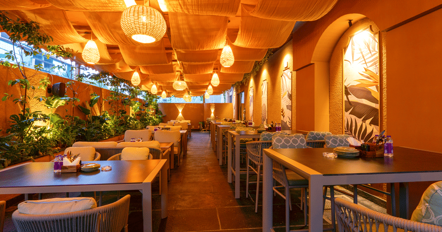 Welcoming entrance and dining space at Cocobrisa with modern furniture, decorative plants, elegant chandeliers, textured walls, and a spacious restaurant interior illuminated with warm lighting.